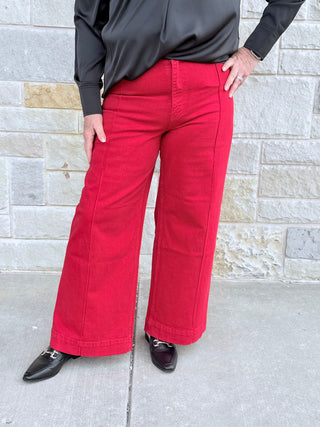 Person wearing red pants and a black top standing against a stone wall.