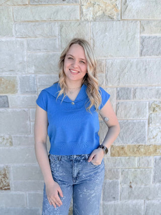 Woman wearing a blue top and jeans standing against a stone wall.