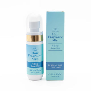 A bottle of Mixologie Hair Fragrance Mist next to its packaging box. The bottle is clear with a white label and gold accents, while the box is blue with product information.