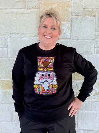 Person wearing a black sweatshirt with a colorful nutcracker design against a stone wall.