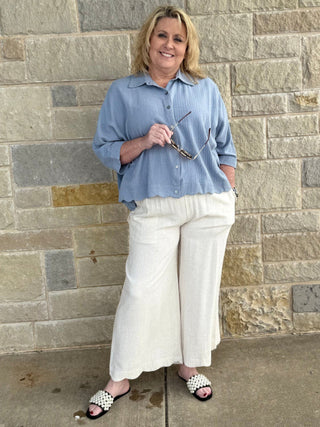 Woman in a blue shirt and white pants standing against a stone wall.