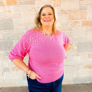 Woman wearing a pink sweater with white polka dots standing against a stone wall.