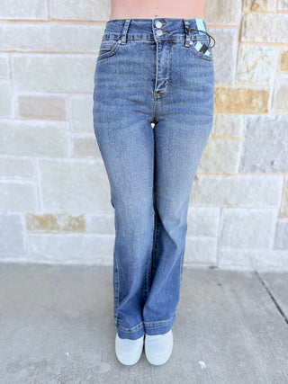 Person wearing blue jeans standing against a brick wall.