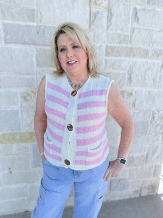 Woman wearing a striped vest and jeans standing against a light stone wall.