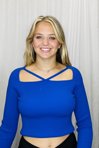Woman wearing a blue long-sleeve top with a criss-cross neckline against a plain background