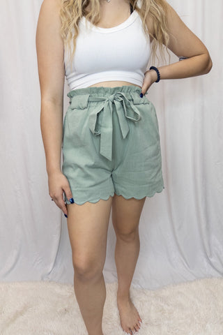 Person wearing a white tank top and green shorts against a plain background