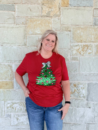 Person wearing a red t-shirt with a Christmas tree design against a stone wall.