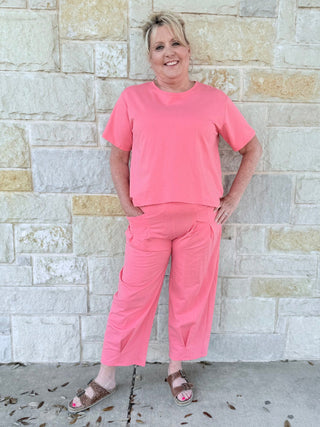 Woman in a pink outfit standing against a stone wall.