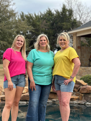Three women standing together by a pool with trees and a house in the background.