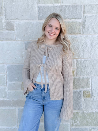 Woman wearing a beige cardigan with a stone wall background