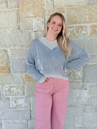 Woman wearing a striped sweater and pink pants standing against a stone wall.