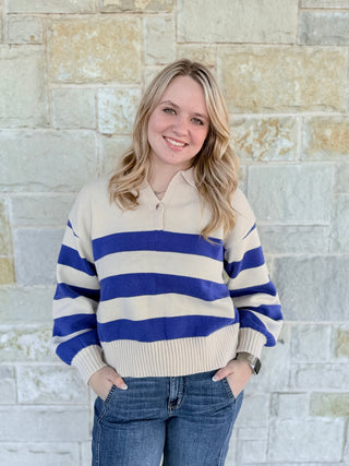 Person wearing a striped sweater and jeans standing against a stone wall.