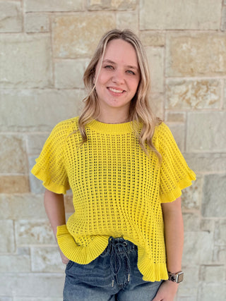 Woman wearing a yellow crochet top standing against a stone wall.