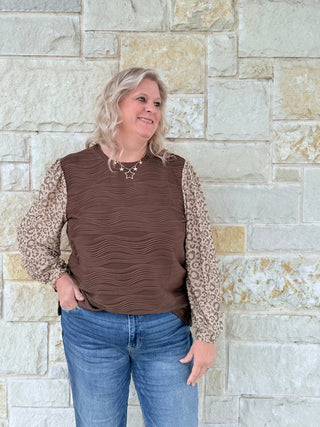 Woman wearing a brown ruched top with leopard print sleeves against a stone wall.