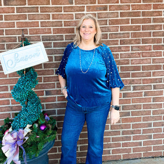 Close-up of a blue velvet top with round neckline and pearl sleeve details.