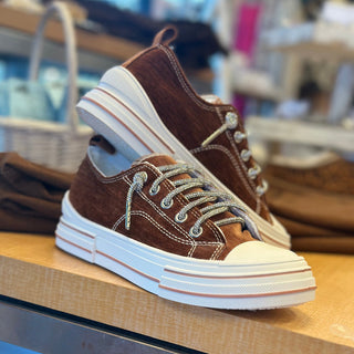 Brown sneaker with white sole on a wooden surface