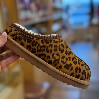 Leopard print slipper held in a hand with a blurred indoor background