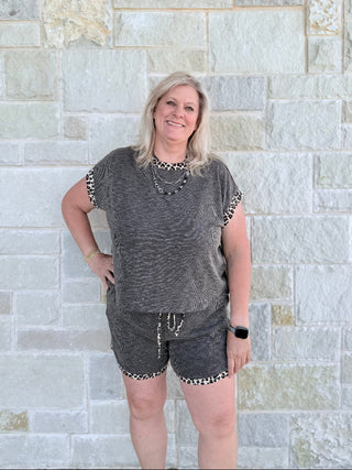 Woman wearing a gray outfit with leopard print details against a stone wall.
