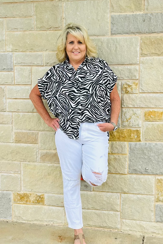 Woman wearing a zebra print top and white pants standing against a stone wall.