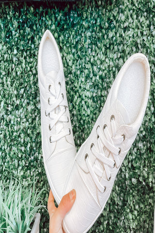 White sneakers held against a green grass background